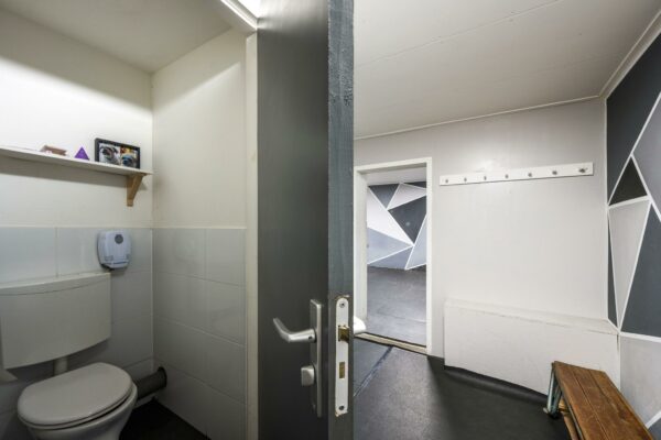 Kleine toiletruimte met open deur naar een kleedkamer in de Albert Cuypstraat, met geometrisch beschilderde muren.